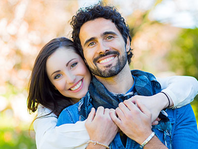 A man and woman embrace each other warmly outdoors during daylight.