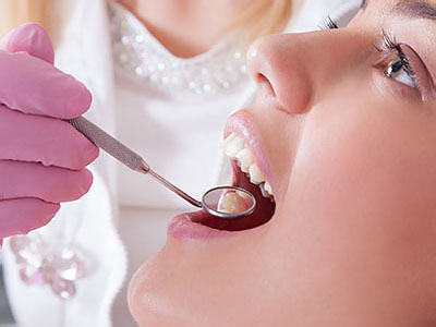 A woman receiving dental care with a dentist using a drill on her teeth.