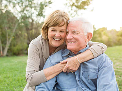 The image shows an older couple embracing each other outdoors during the daytime.