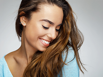 A woman with long hair and a radiant smile, wearing a light blue top, against a neutral background.