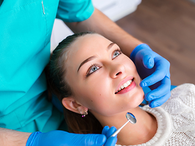 The image shows a dental professional performing a procedure on a patient s teeth while the patient smiles and looks towards the camera.