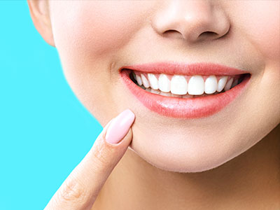 A close-up image of a smiling person with a toothy grin, showcasing their well-maintained teeth, against a blue background.